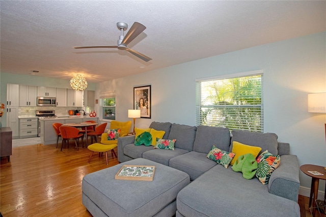 living area with light wood-type flooring, a textured ceiling, and ceiling fan with notable chandelier