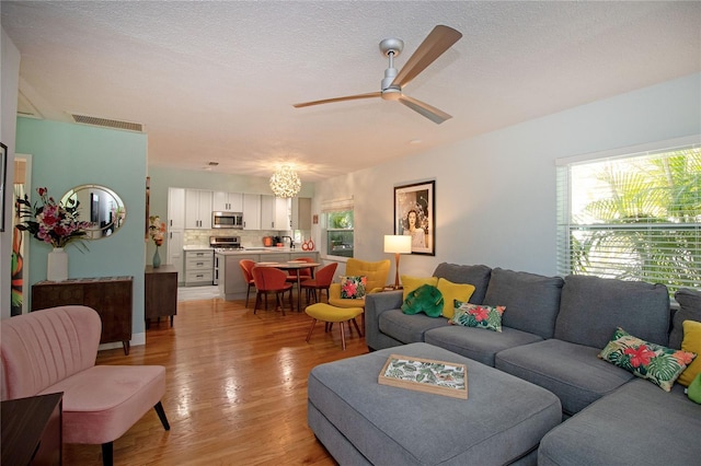 living room featuring visible vents, a textured ceiling, light wood-style flooring, and ceiling fan with notable chandelier