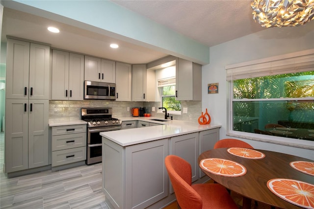 kitchen with a peninsula, gray cabinetry, appliances with stainless steel finishes, and a sink