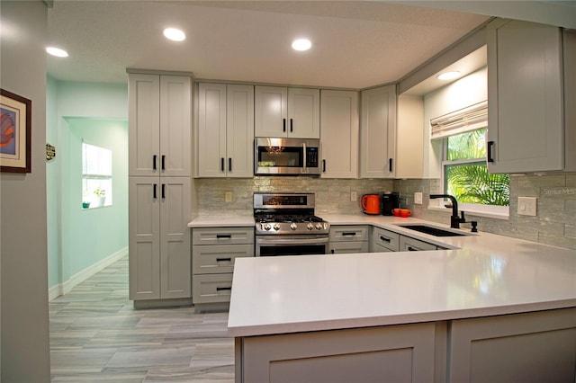 kitchen with gray cabinetry, stainless steel appliances, light countertops, and a sink