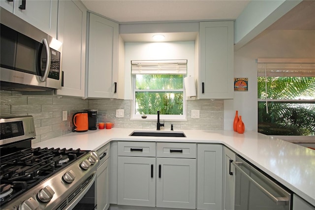 kitchen featuring light countertops, backsplash, appliances with stainless steel finishes, and a sink