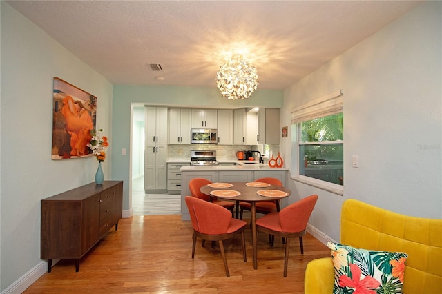 dining area with baseboards, visible vents, a chandelier, and light wood-type flooring