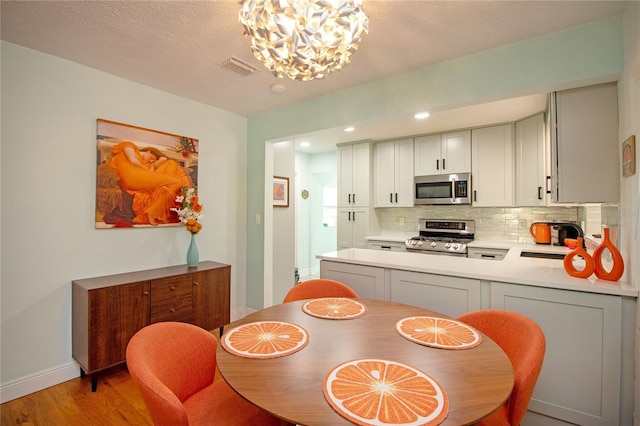 dining room with light wood finished floors, visible vents, baseboards, an inviting chandelier, and a textured ceiling