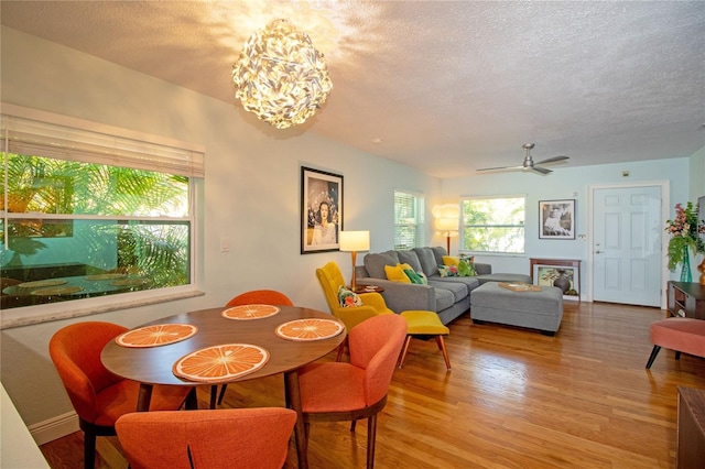 dining area with ceiling fan with notable chandelier, light wood-type flooring, and a textured ceiling