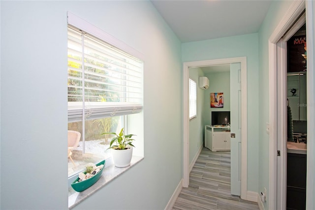 corridor with light wood-style flooring, baseboards, and a wall unit AC