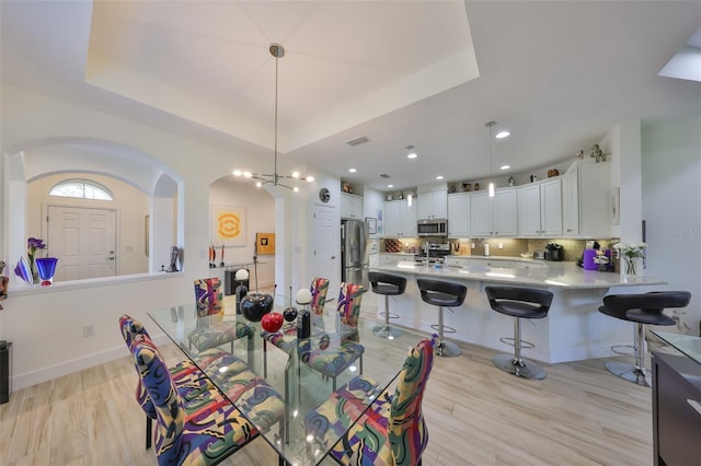 807 Chipper Dr, Sun City Center, FL 33573 - dining room featuring visible vents, light wood-style flooring, baseboards, arched walkways, and a raised ceiling