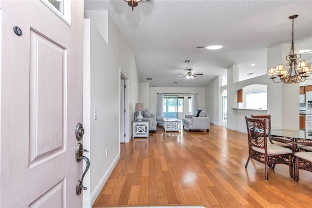 entryway featuring baseboards, light wood-style flooring, ceiling fan with notable chandelier, arched walkways, and a textured ceiling