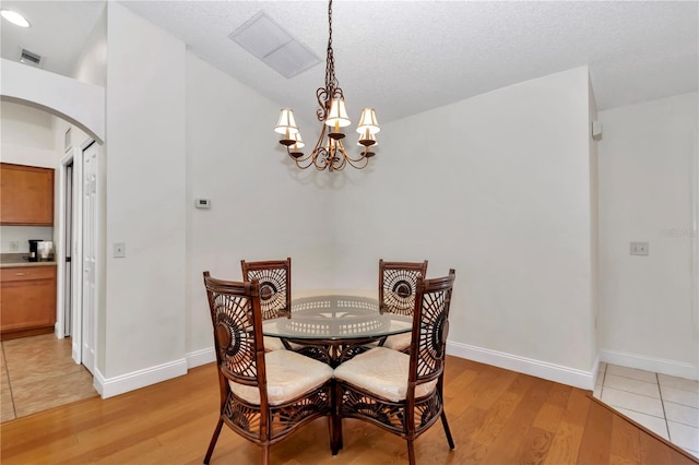 dining area with arched walkways, visible vents, light wood finished floors, and a notable chandelier