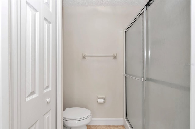 bathroom with tile patterned flooring, a shower stall, baseboards, toilet, and a textured ceiling