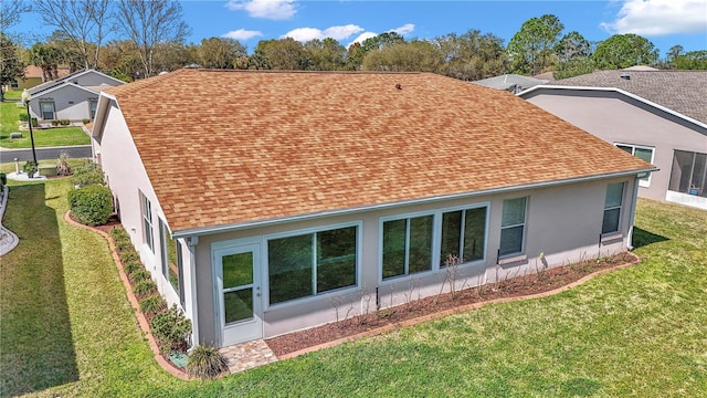 rear view of house featuring stucco siding, a yard, and a shingled roof