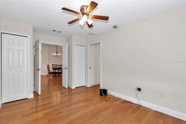 spare room featuring visible vents, light wood-style flooring, ceiling fan with notable chandelier, a textured ceiling, and baseboards