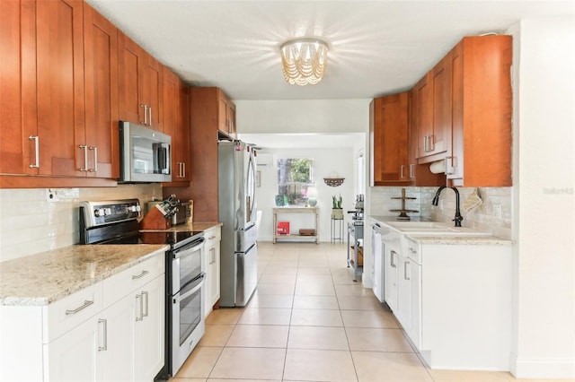 kitchen featuring brown cabinets, a notable chandelier, a sink, stainless steel appliances, and light tile patterned floors