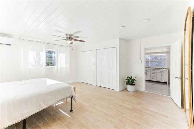 bedroom featuring baseboards, multiple closets, an AC wall unit, and light wood-style flooring