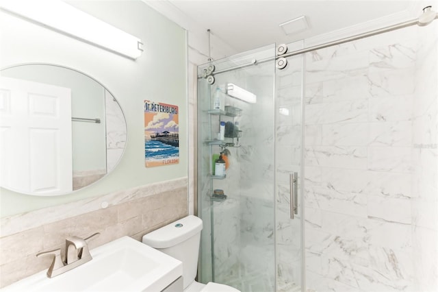 full bathroom with a marble finish shower, tile walls, toilet, wainscoting, and vanity