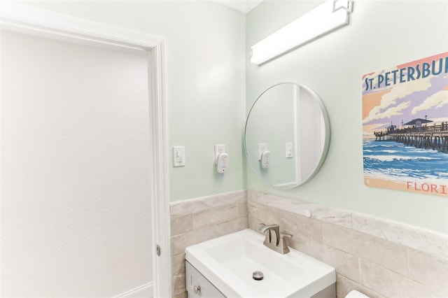 half bathroom featuring wainscoting, tile walls, and vanity