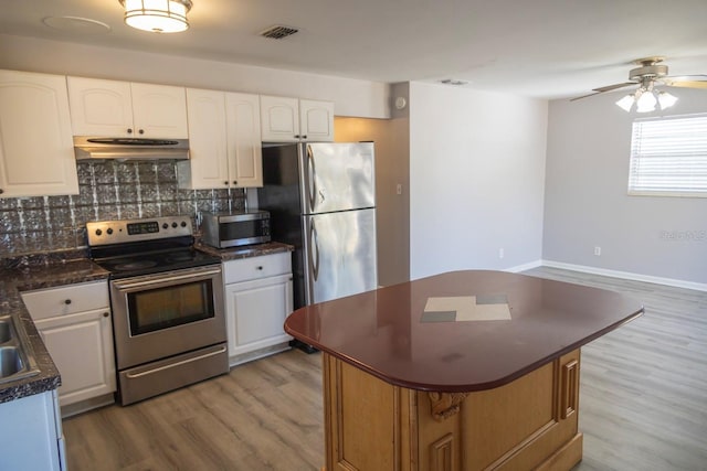 kitchen featuring under cabinet range hood, backsplash, dark countertops, appliances with stainless steel finishes, and light wood finished floors