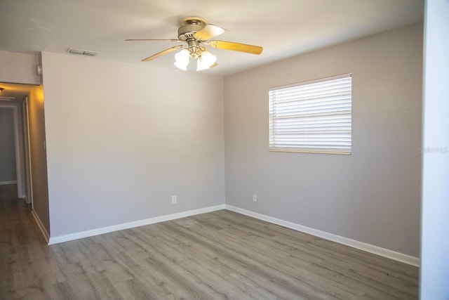 unfurnished room with wood finished floors, a ceiling fan, baseboards, and visible vents