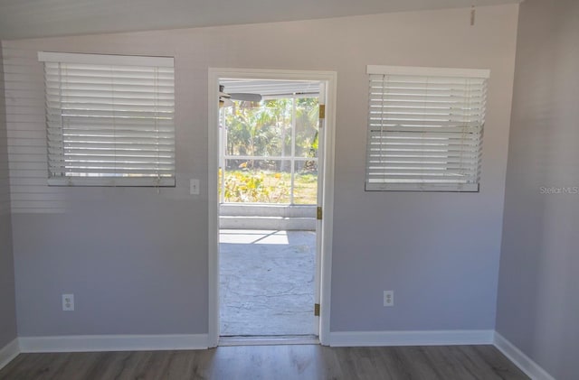 doorway featuring lofted ceiling, baseboards, and wood finished floors