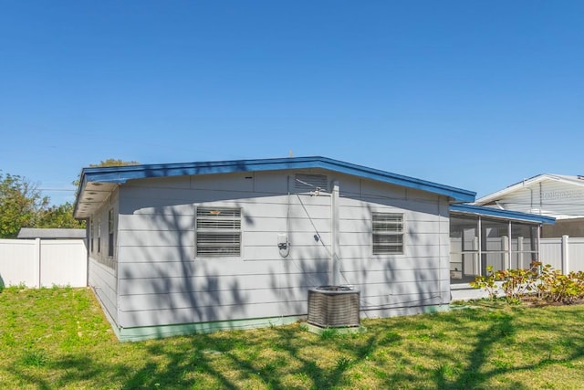 view of property exterior with central AC, fence, a yard, and a sunroom