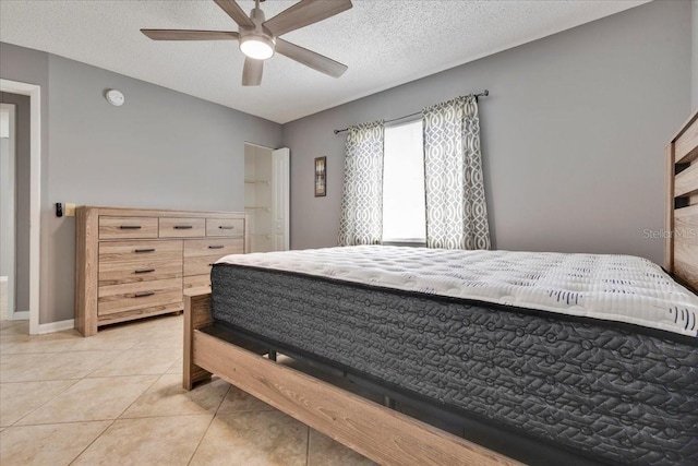 bedroom with ceiling fan, light tile patterned floors, baseboards, and a textured ceiling