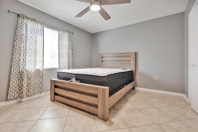 bedroom featuring light tile patterned floors, a ceiling fan, baseboards, and a textured ceiling