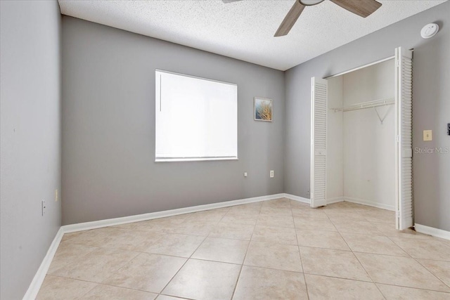 unfurnished bedroom with tile patterned floors, a textured ceiling, a closet, baseboards, and ceiling fan