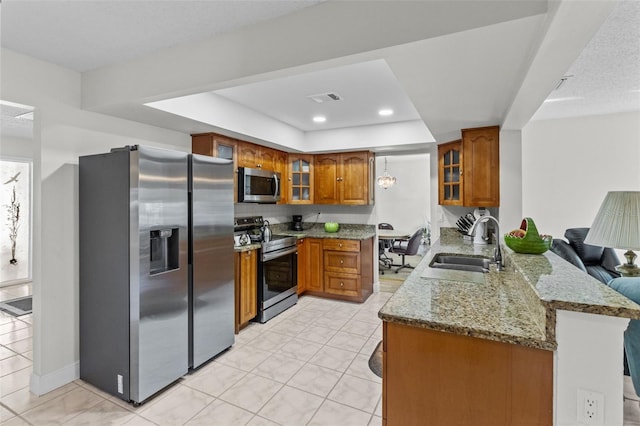 kitchen featuring visible vents, a peninsula, a sink, appliances with stainless steel finishes, and brown cabinets