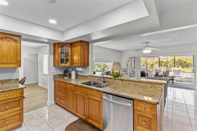 kitchen featuring dishwasher, light tile patterned floors, brown cabinets, a peninsula, and a sink