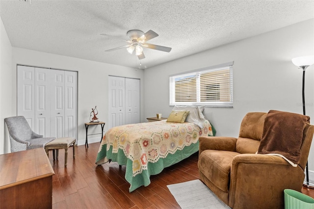 bedroom with a ceiling fan, baseboards, wood finished floors, multiple closets, and a textured ceiling