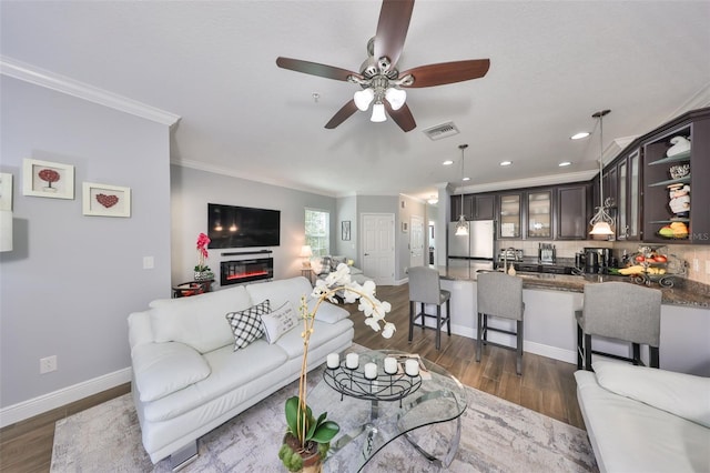 living room with visible vents, dark wood-type flooring, ceiling fan, baseboards, and ornamental molding