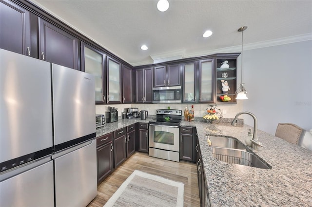 kitchen featuring ornamental molding, a sink, light stone counters, light wood-style floors, and appliances with stainless steel finishes