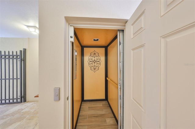 hall featuring elevator, light wood-style flooring, and a textured ceiling