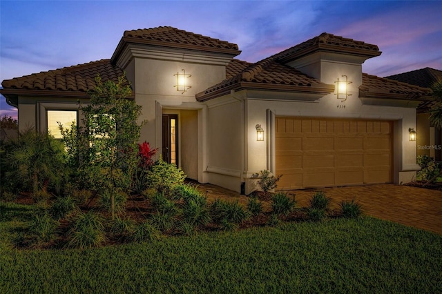 mediterranean / spanish-style house featuring stucco siding, a tiled roof, decorative driveway, and a garage