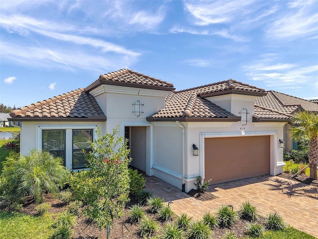 mediterranean / spanish-style house featuring a tile roof, an attached garage, driveway, and stucco siding