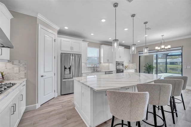 kitchen with ornamental molding, a sink, a center island, white cabinetry, and appliances with stainless steel finishes