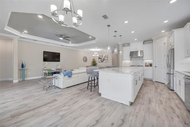 kitchen featuring tasteful backsplash, under cabinet range hood, open floor plan, appliances with stainless steel finishes, and a raised ceiling