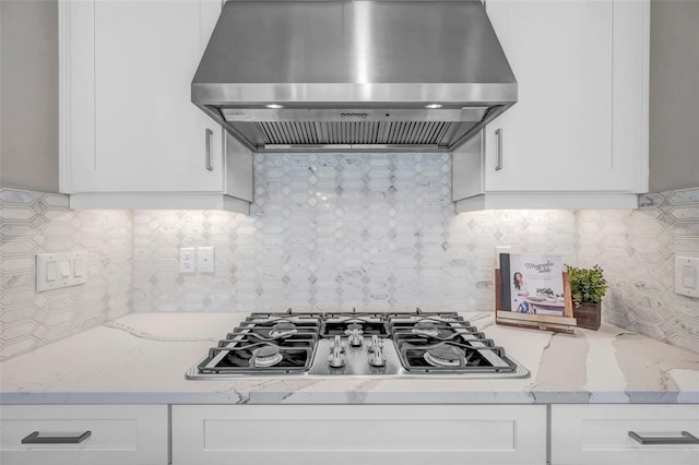 kitchen featuring stainless steel gas cooktop, light stone counters, decorative backsplash, white cabinets, and wall chimney exhaust hood