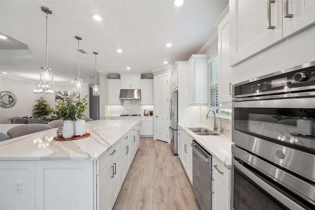 kitchen with a kitchen island, ornamental molding, a sink, under cabinet range hood, and appliances with stainless steel finishes