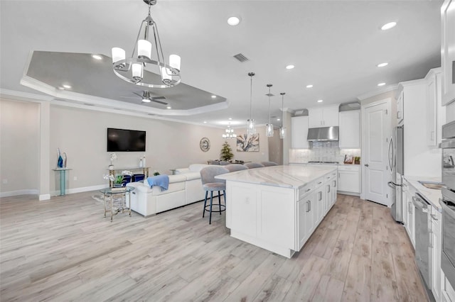 kitchen featuring visible vents, a tray ceiling, under cabinet range hood, ceiling fan with notable chandelier, and open floor plan