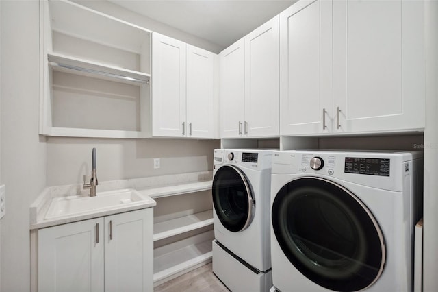 laundry room featuring cabinet space, washing machine and dryer, light wood finished floors, and a sink