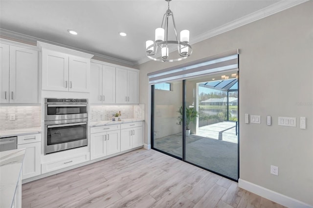 kitchen with ornamental molding, backsplash, appliances with stainless steel finishes, white cabinets, and a chandelier