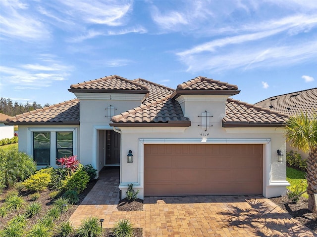 mediterranean / spanish-style house featuring decorative driveway, a tiled roof, an attached garage, and stucco siding