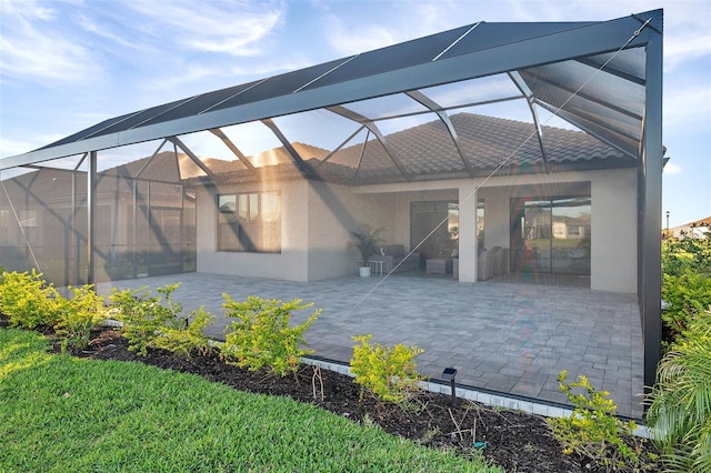 rear view of house with a patio area, stucco siding, a tiled roof, and glass enclosure