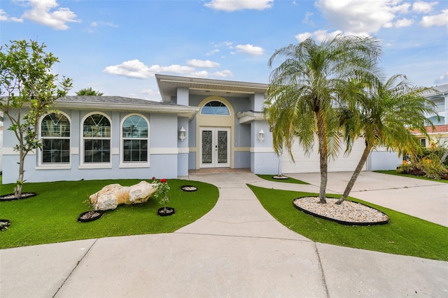 view of front facade with a front lawn, french doors, driveway, and stucco siding