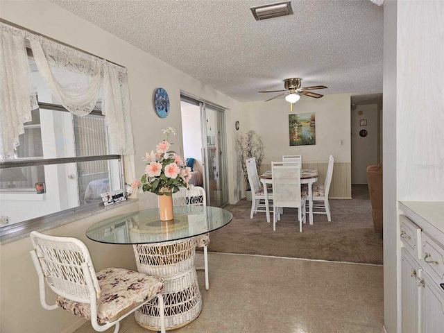 carpeted dining area with a textured ceiling, visible vents, and ceiling fan