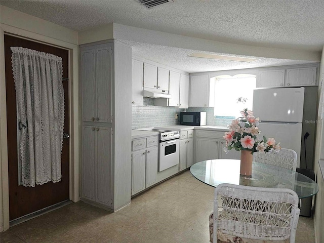 kitchen with under cabinet range hood, light floors, light countertops, decorative backsplash, and white appliances