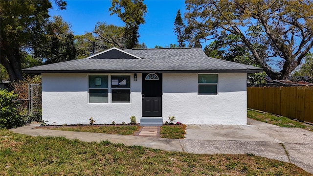 bungalow-style house featuring a patio, fence, roof with shingles, stucco siding, and a front lawn