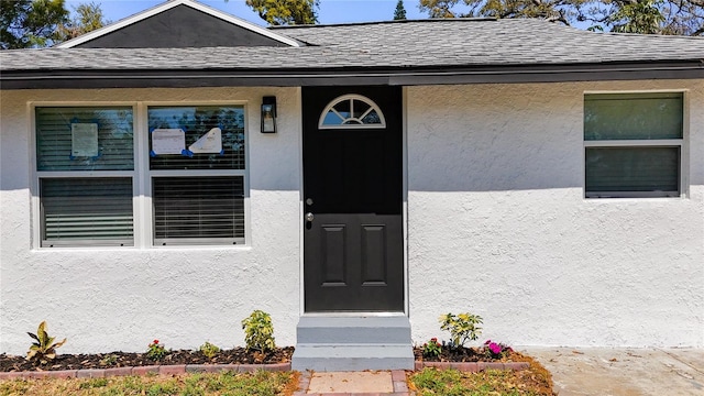 entrance to property with stucco siding and roof with shingles