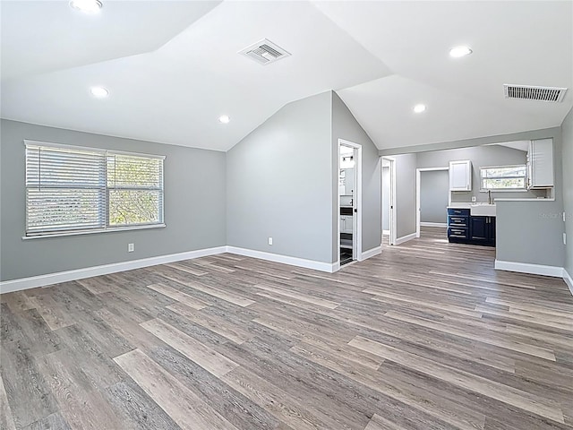 unfurnished living room featuring a sink, visible vents, lofted ceiling, and wood finished floors