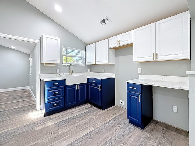 kitchen featuring visible vents, blue cabinetry, lofted ceiling, light wood-style flooring, and a sink